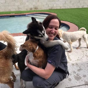 vet team member getting a hug from a dog while outside by the dog pool