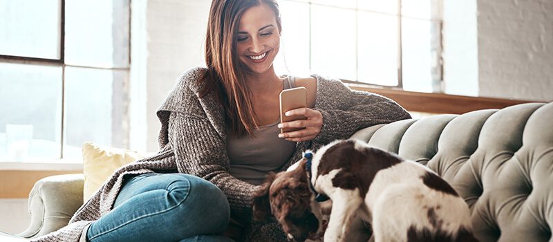 a woman sitting on a couch next to a dog while looking at her phone